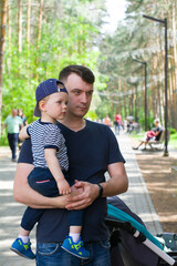 the father holds the little son in his arms and both look forward, dissatisfied, tense, waiting for the mother. Walk in the Park in nature. Family holiday