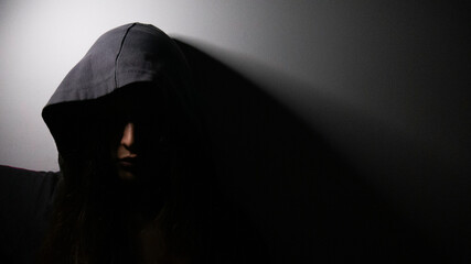 A woman with a hood over her head in the dark. Critical state of mind and spirit.