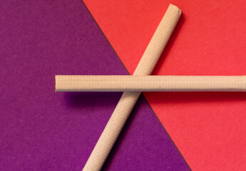 Two cigarettes forming a cross shape on the border of pink and purple backgrounds