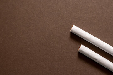 Two cigarette end laying flat on a brown background. Left area empty for copyspace