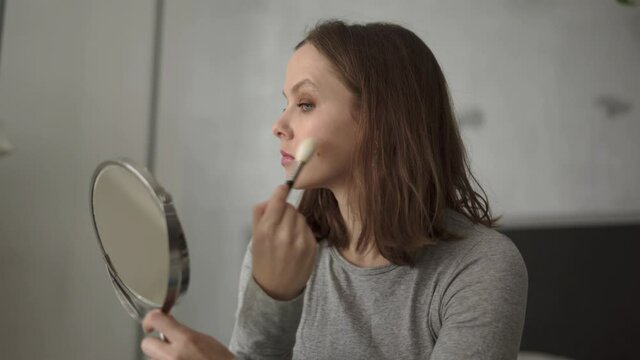 Woman holding makeup brush applying makeup on her face