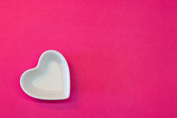 White ceramic heart shaped plate on a simple pink background from above