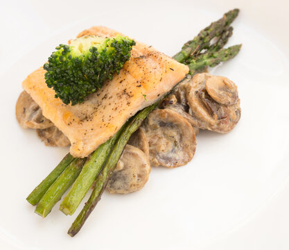 dish of fried river trout fillet with garnish of broccoli, asparagus sprouts and mushroom sauce on white background