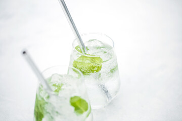 Beautiful glass of water or mojito with lime and mint cocktail on the gree background and white table summer vibe and atmosphere