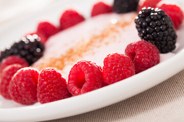 raspberries and blackberries laid out on a white plate in circle with yogurt and cinnamon
