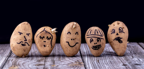 Funny potato with a painted face on a wooden table and on a black background. Young potatoes on the table for cooking.