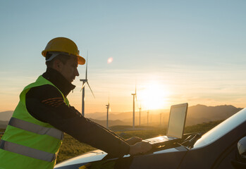 Technician Engineer in Wind Turbine Power Generator Station checks the status of the turbines using a laptop © bigguns