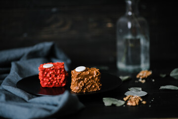 two red and chocolate cupcakes on a black plate against the background of a vase