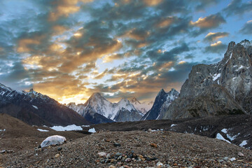 Schöne Aussicht auf Gasherbrum und Mitre Peak mit dramatischen Wolken bei Sonnenaufgang mit einem provisorischen Unterschlupf aus Steinen und einer Plastikabdeckung, K2 Base Camp Trek, Baltoro-Gletscher, Karakorum, Pakistan