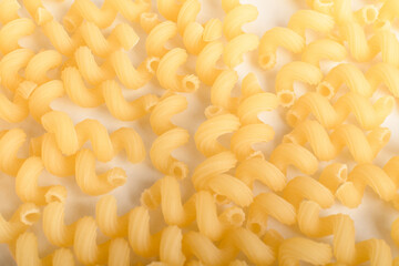 Heap of dried serpentelli Italian pasta in a round bowl ready to be cooked, isolated on a white table, top view or flat lay of healthy food 
