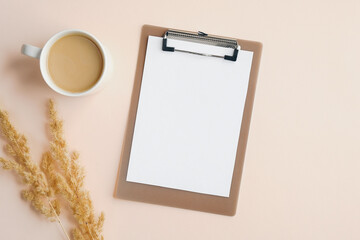 Flat lay composition with cup of coffee, blank paper clipboard, dry flowers on beige background....