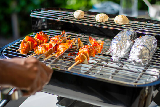 Grilling on a hybrid grill barbecue for electric or charcoal. Marinated raw chicken skewers on wooden skewers with bell pepper and onion in a satay marinade. Corn on the cob in aluminum foil.