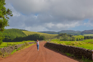 Young woman walk at country road. Fields with blue sky. Terceira