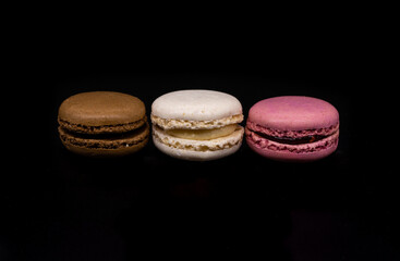 Colored macaroons, French cookies isolated on a black background. Brown white and pink cookies, biscuits
