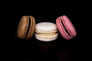 Colored macaroons, French cookies isolated on a black background. Brown white and pink cookies, biscuits