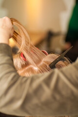Hairdresser curling a blond woman's hair in professional hairdressing salon or barbershop , seen from behind the customer, unrecognizable.