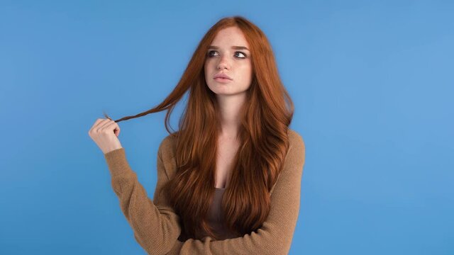 Red-haired female in brown t-shirt and cardigan. She looking thoughtful, came up with an idea, smiling while posing against blue background. Close up