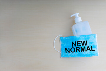 NEW NORMAL text with face mask and hand sanitizer on wooden background. Covid 19 and coronavirus...