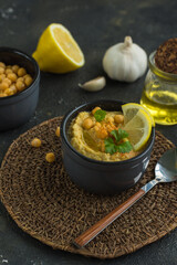 Hummus is a traditional snack made from chickpea puree and the products it is made from-chickpeas, lemon, garlic and olive oil on a dark background