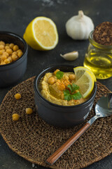 Hummus is a traditional snack made from chickpea puree and the products it is made from-chickpeas, lemon, garlic and olive oil on a dark background