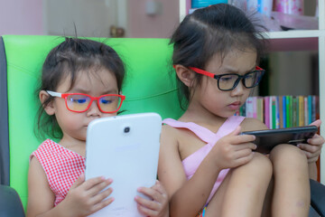 Two kindergarten Asian girls are playing phones and tablets with fun.