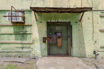 Large metal door on side of abandoned brick factory painted green with metal gate