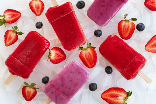 Popsicle with berries on ice cubes. Homemade ice cream with strawberry and blueberry on light background. Refreshing summer dessert, vegan food. Top view, flat lay