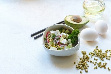 Salad for a balanced diet of sprouts, tofu, radishes and avocado and mini greens in a white bowl with chopsticks, white background with space