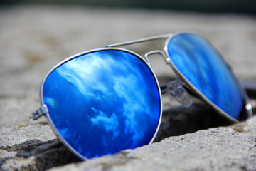 Blue sunglasses on the stone withe reflection from sun and clouds