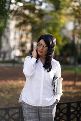 Autumn fashion outdoor. The girl in fashionable stylish white shirt , pants and sunglasses, autumnal lifestyle on the background of blurry yellow-green trees in the park. Vertical
