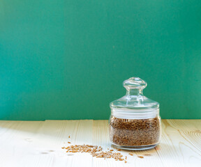 Dry grits spelt in a small glass jar on a bright aquamarine background with space