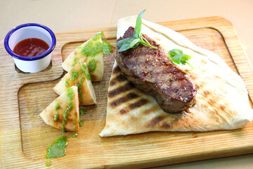 Medium-roasted steak cut into pieces on a wooden board with sauce and seasonings. Delicious steak. Beef steak medium rare on vegetable cushion. Beef steak on wooden plate.