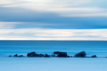 Fototapeta na wymiar Rocks laying in the ocean with an cloudy sunset as background outside island of Gotland in Sweden