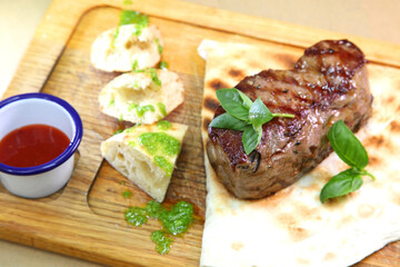 Medium-roasted steak cut into pieces on a wooden board with sauce and seasonings. Delicious steak. Beef steak medium rare on vegetable cushion. Beef steak on wooden plate.