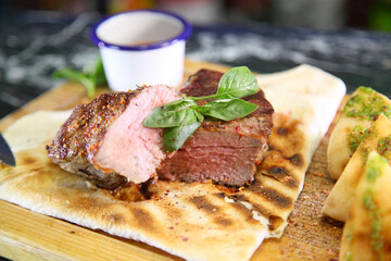 Medium-roasted steak cut into pieces on a wooden board with sauce and seasonings. Delicious steak. Beef steak medium rare on vegetable cushion. Beef steak on wooden plate.