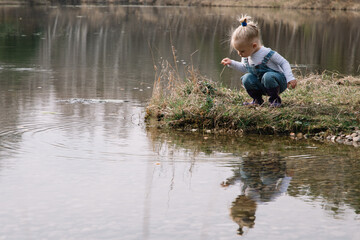 Little girl in rubber boots catches and feeds fish on the river in a jar