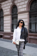 Fototapeta premium Autumn fashion outdoor. The girl in fashionable stylish white shirt , pants, jacket and sunglasses, autumnal lifestyle on the background of blurry yellow-green trees in the park. Vertical