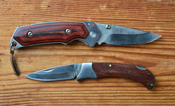 close-up of two folding knives with wooden handles in the open state isolated on on a brown wooden background