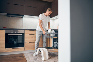 Concentrated mature man putting dishes into dishwasher