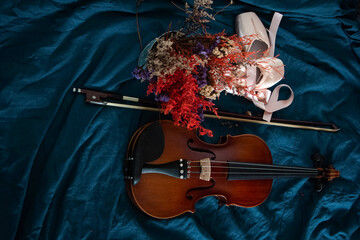 Violin and bow put beside dried flower pot and ballet shoes,on background