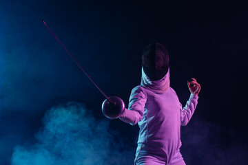 Low angle view of swordswoman fencing on black background with smoke and lighting