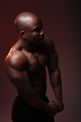 Portrait of a professional dark-skinned boxer with a naked torso with his arms crossed in the abdomen with red backlight