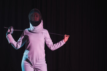 Swordswoman in fencing mask holding rapier isolated on black with copy space