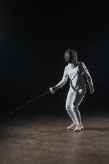 Fototapeta na wymiar Swordswoman in fencing suit and mask training with rapier on black background