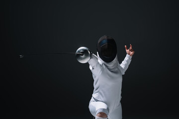 Fencer in fencing mask exercising with rapier isolated on black