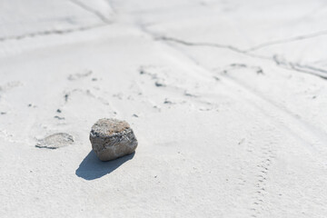 closeup photo of the white cracked soil of the bottom of the lake with the small stone casting a long shadow at the foreground and blurry background perspective