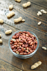 unshelled peanuts in a glass plate on a wooden background. peeled peanuts are scattered nearby. traditional beer snack. place for text.