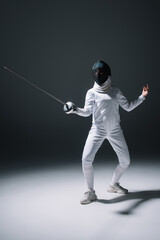 Fototapeta na wymiar Fencer in fencing mask training with rapier on white surface on black background