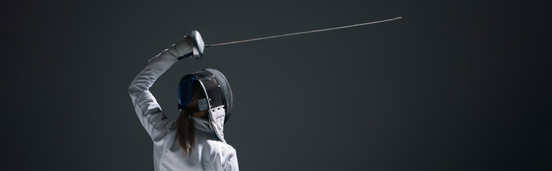 Back view of fencer training with rapier isolated on black, panoramic crop