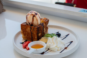 Close up Honey Toast serve with Vanilla ice-cream, Whip cream, Sliced bananas, and strawberries on the white plate.